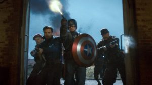 A scene from "Captain America: The First Avenger" (2011). Captain America, shield in hand, bursts into a door with his team, guns literally blazing.